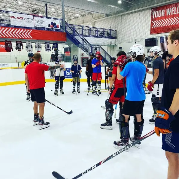 Zdjecie trenera hokejowego i graczy na hokejowym lodowisku syntetycznym
